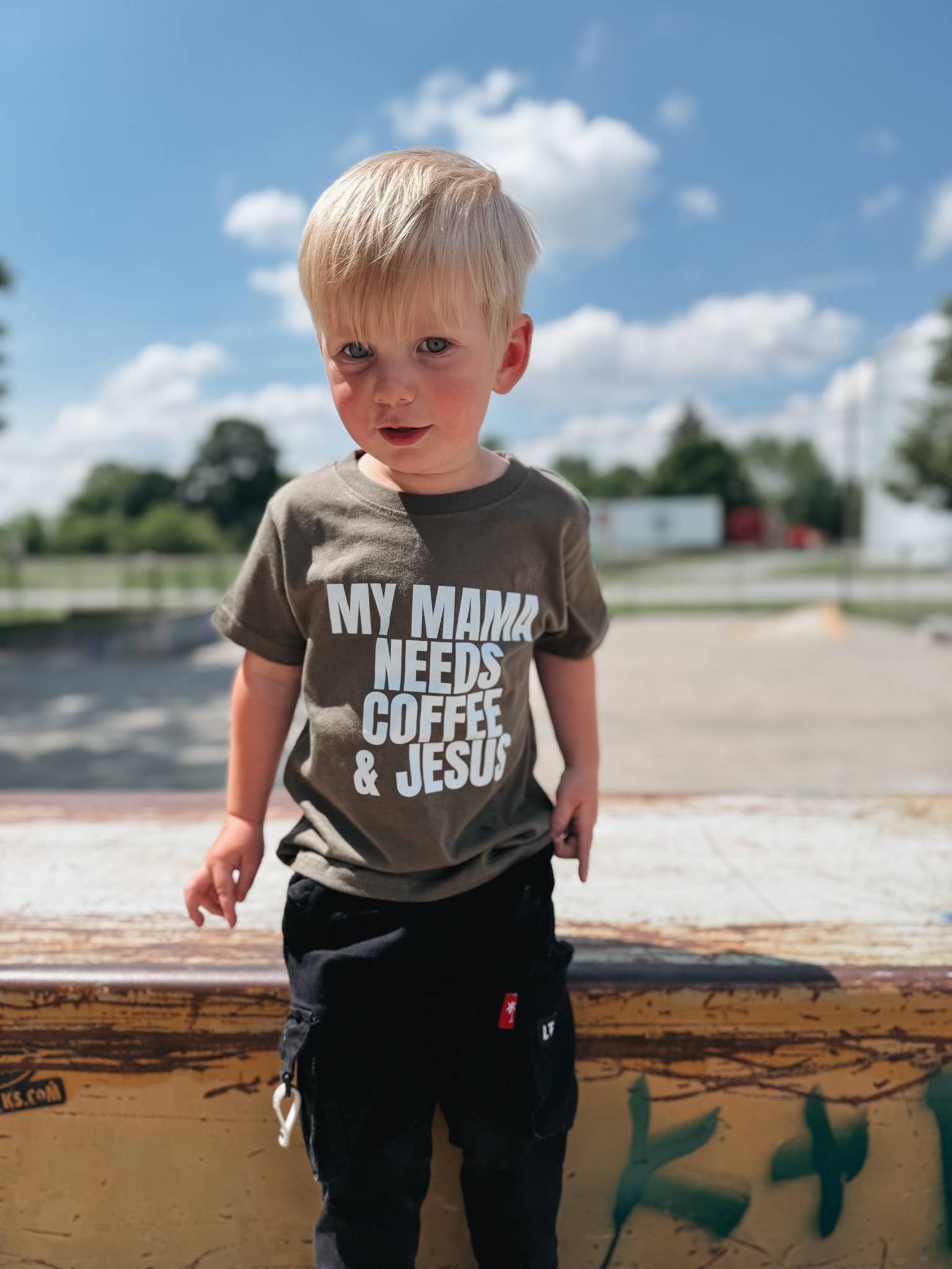 Child wearing a t-shirt with text standing outdoors on a sunny day