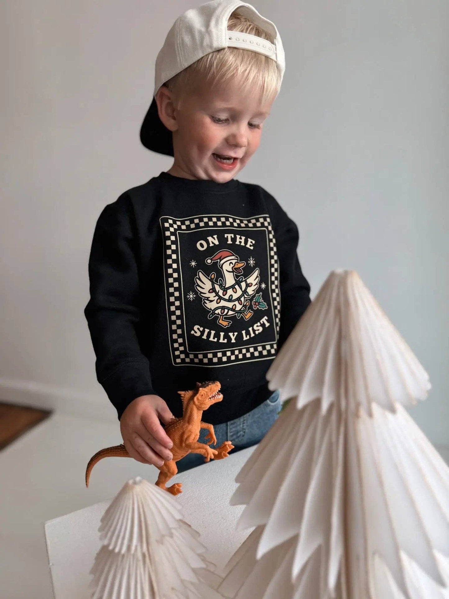 Child wearing a black sweatshirt with a graphic design, standing next to paper mountains.