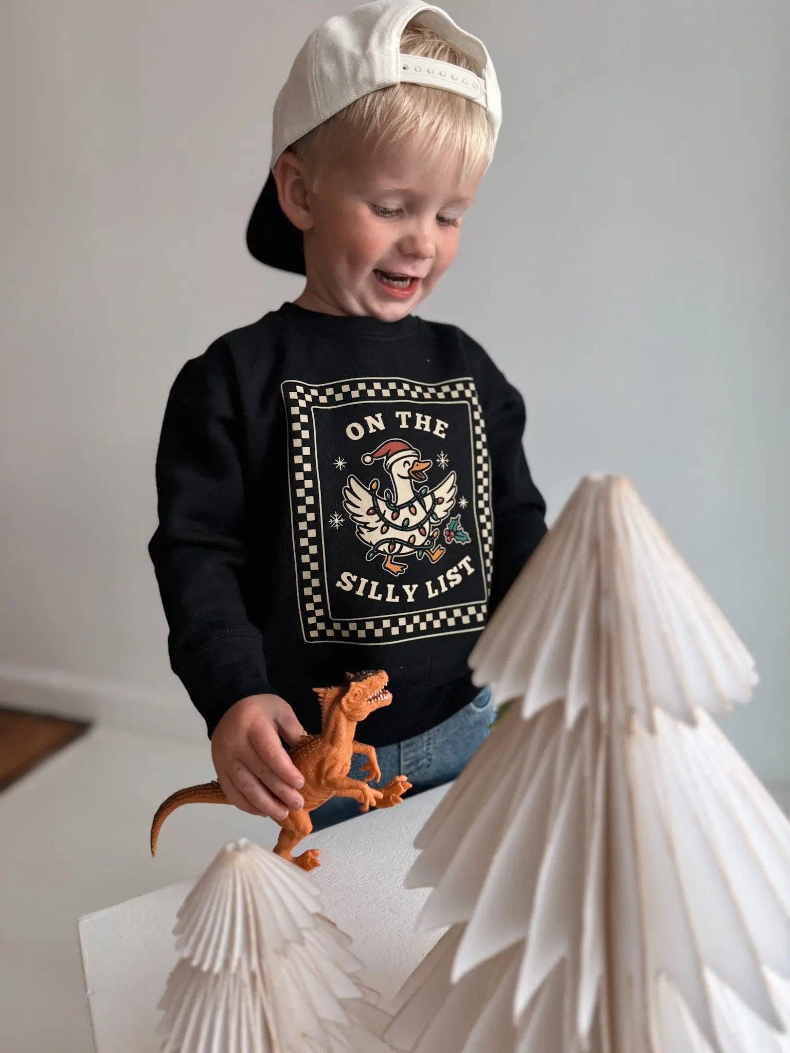 Child wearing a black sweatshirt with a graphic design, standing next to paper mountains.