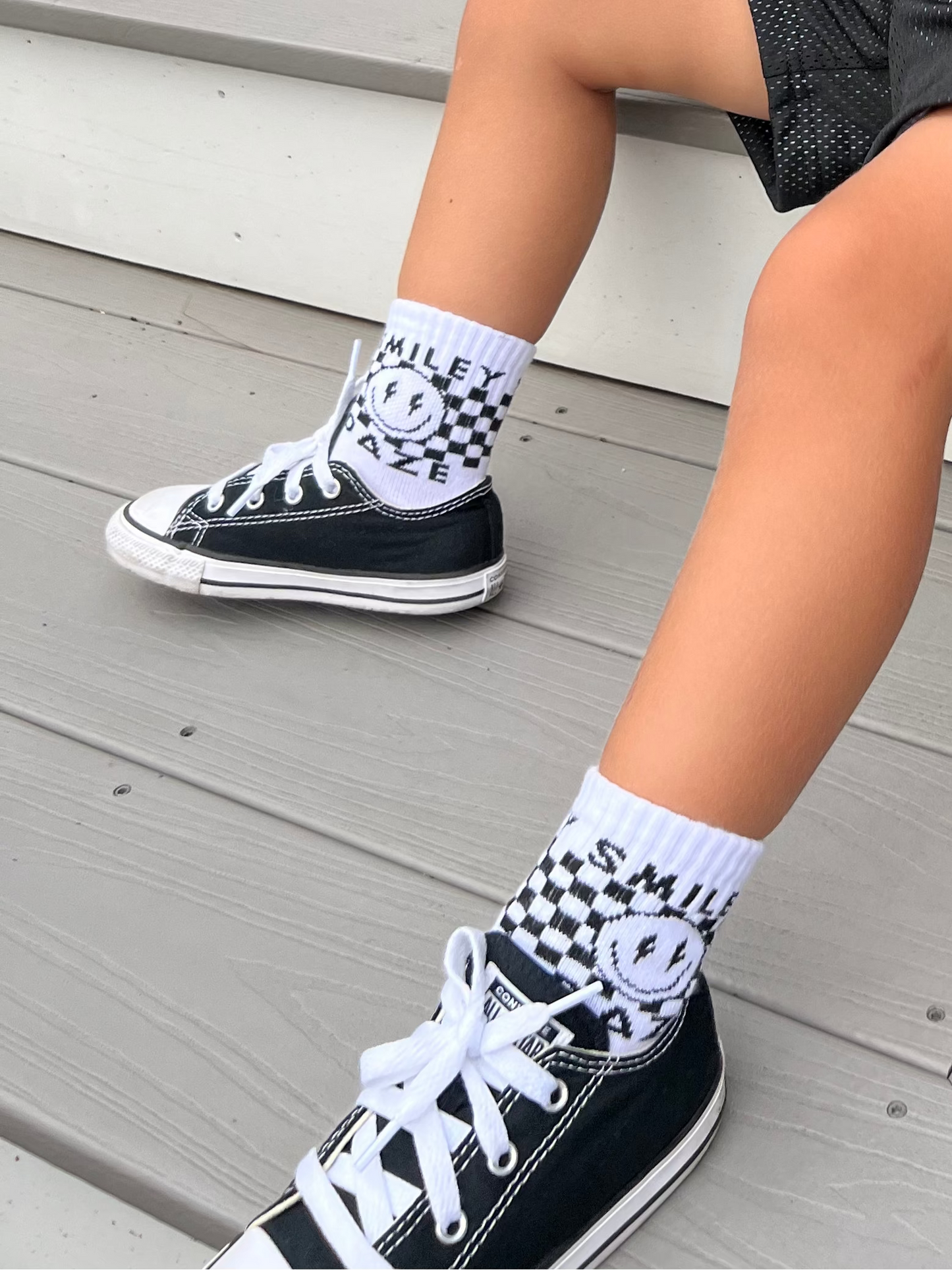 Person wearing black high-top sneakers with white soles and checkered socks on a wooden floor.
