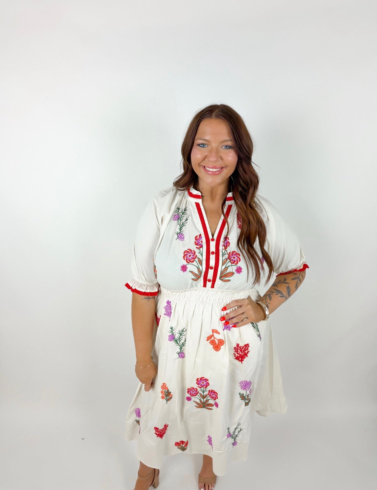 Woman wearing a white dress with floral embroidery on a plain background