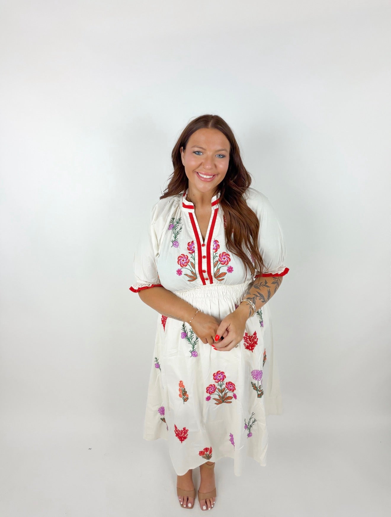 Woman wearing a white dress with floral embroidery on a plain background