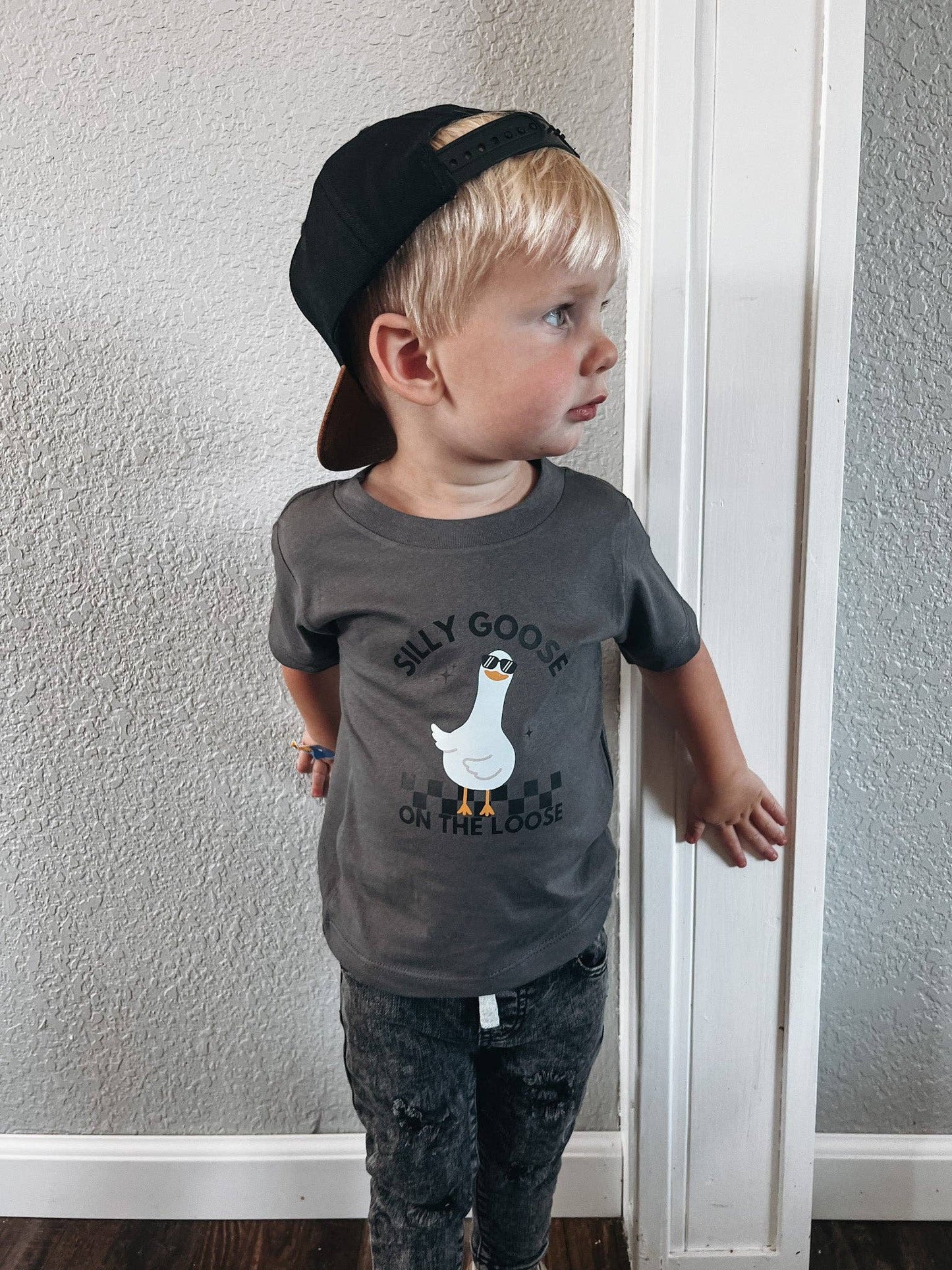 Child wearing a gray t-shirt with a graphic design and text, standing against a plain wall.