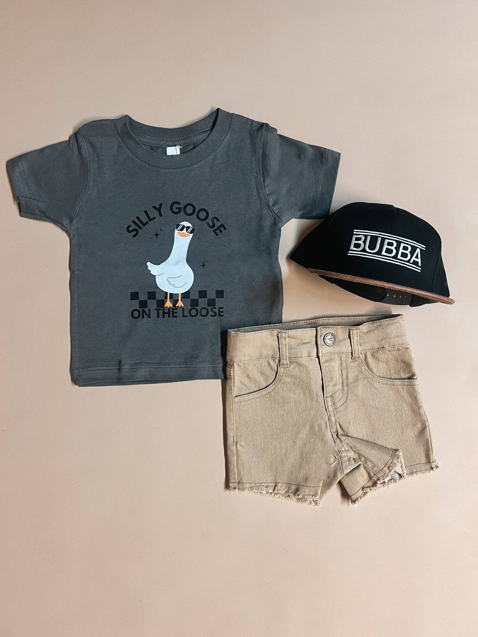 Children's t-shirt with graphic design, shorts, and cap on a beige background