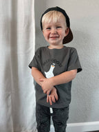 Child wearing a gray t-shirt with a graphic design and text, standing against a plain background.